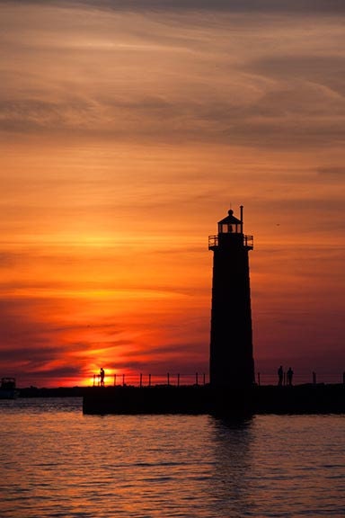A Lone Fisherman and the Muskegon Lighthouse are Silhouetted by the Setting Sun Fine Art Photo
